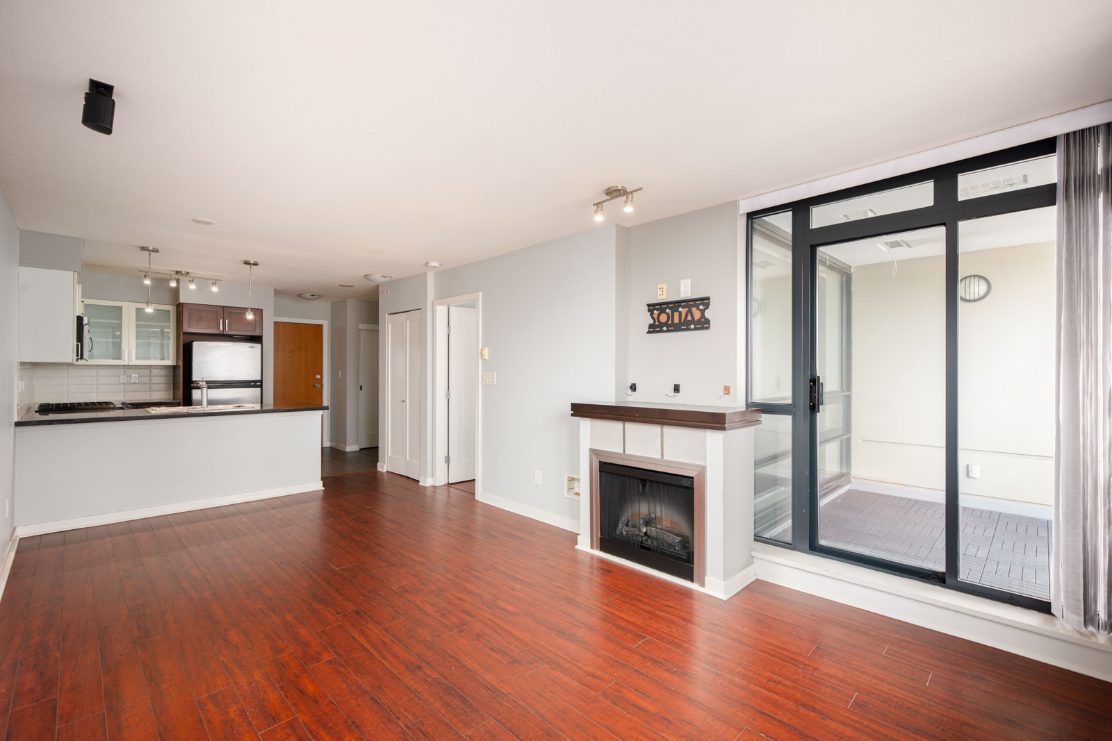 Unfurnished open-plan apartment with hardwood floors, a modern kitchen, a fireplace, and sliding glass doors leading to an enclosed balcony.