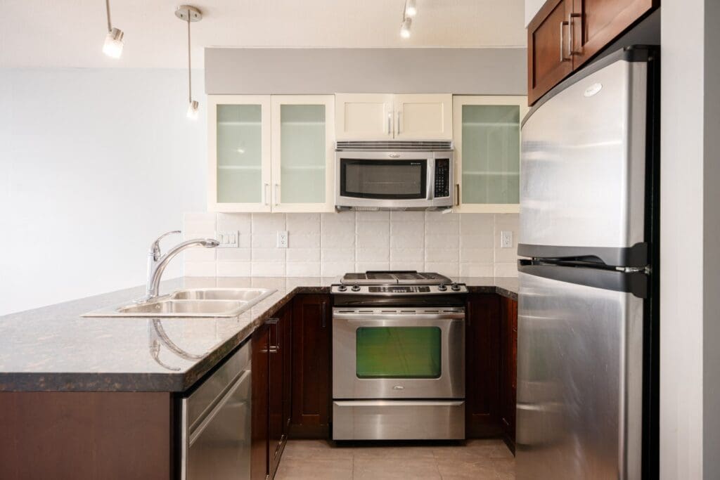 Modern kitchen with stainless steel appliances, dark wood cabinets, a double sink, microwave, and a tiled backsplash under track lighting.