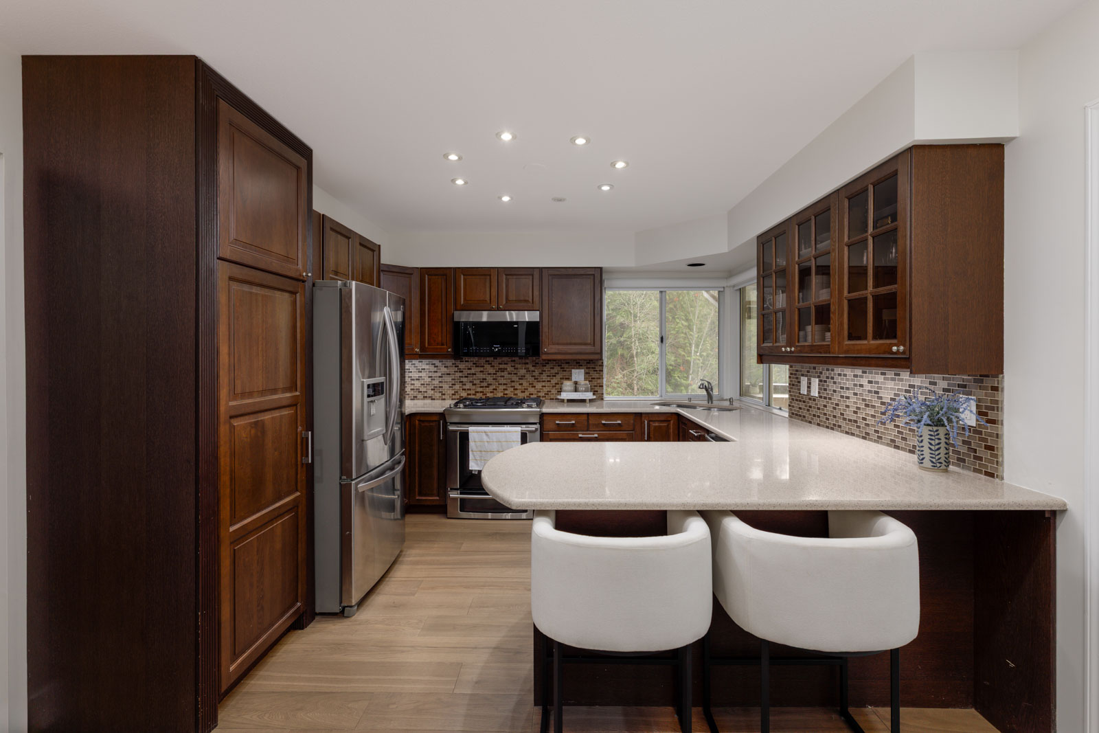 Modern kitchen with dark wood cabinets, stainless steel appliances, a mosaic tile backsplash, and a peninsula with two white barstools.