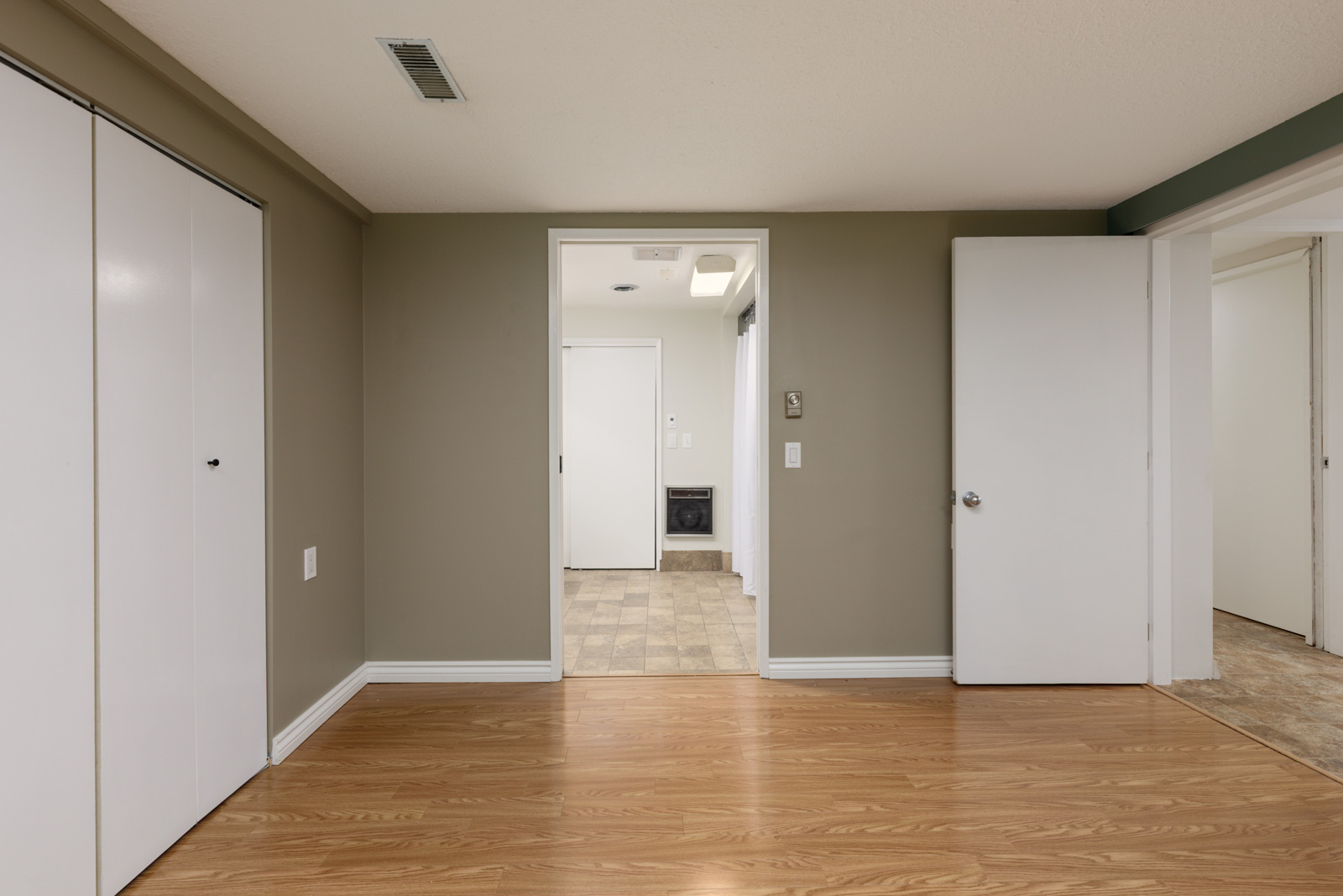 A room with light wood flooring, olive green and white walls, white closet doors, and an open doorway leading to a laundry area with a washer visible in the background.