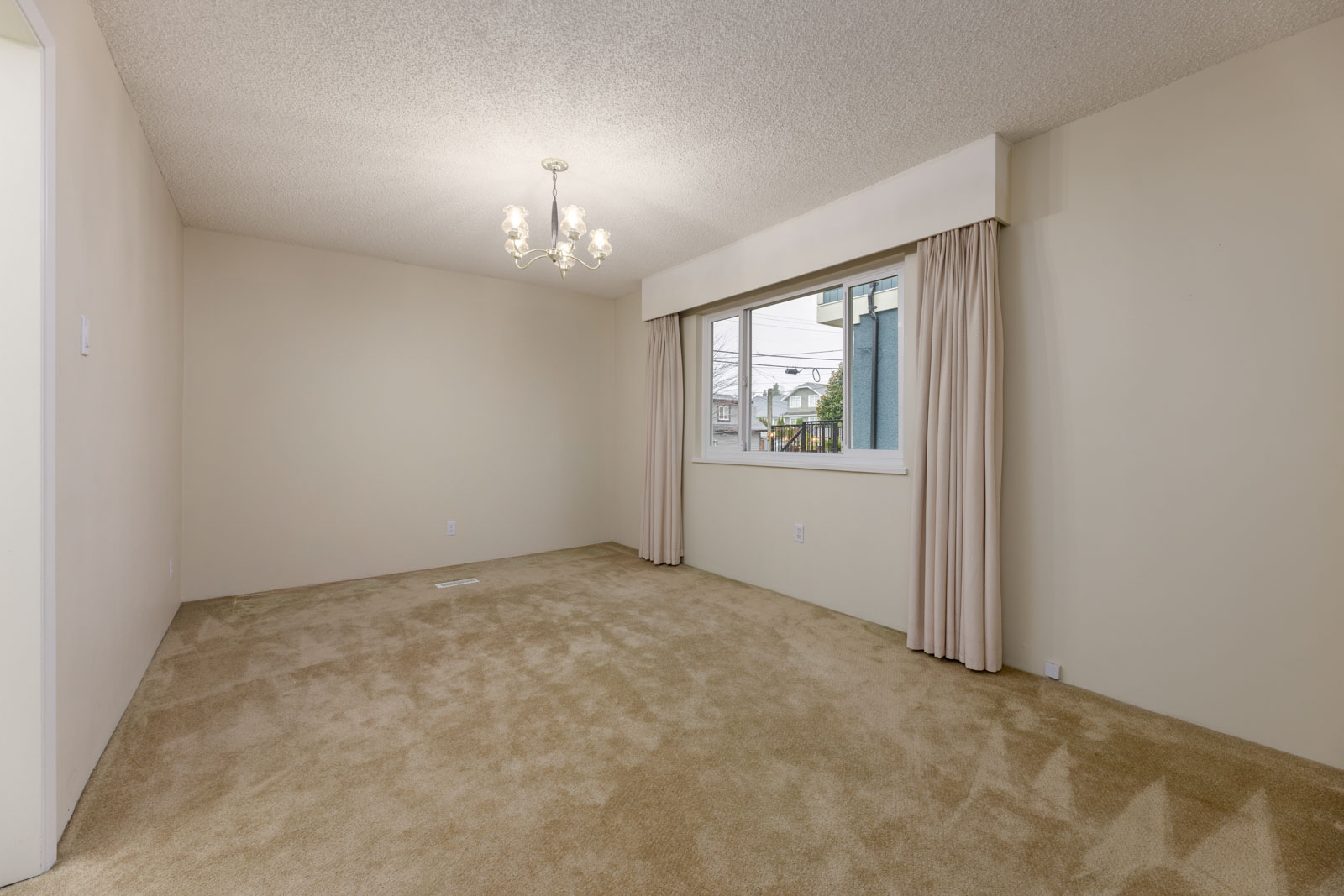 Empty room with beige carpet, cream-colored walls, a window with curtains, and a ceiling light fixture.
