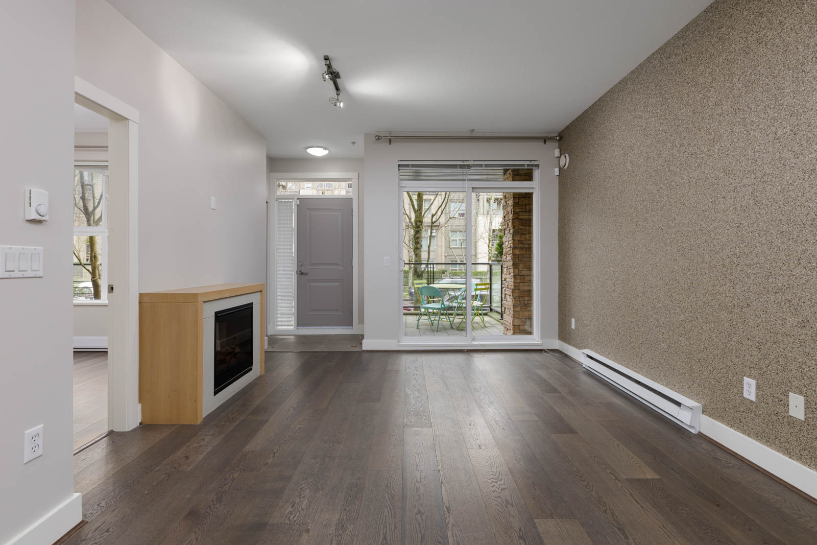 Unfurnished living room with hardwood floors, electric fireplace, large window, glass sliding doors to a patio, and a feature wall with baseboard heater.