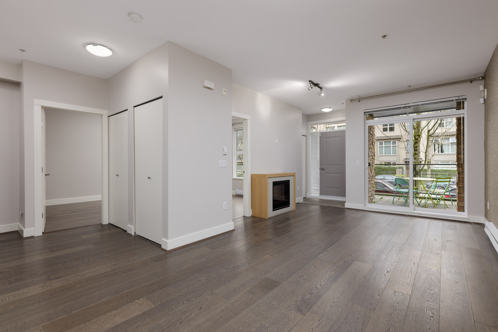 Unfurnished living room with large windows, dark wood floors, a fireplace, and white walls. Multiple doorways lead to adjacent rooms.