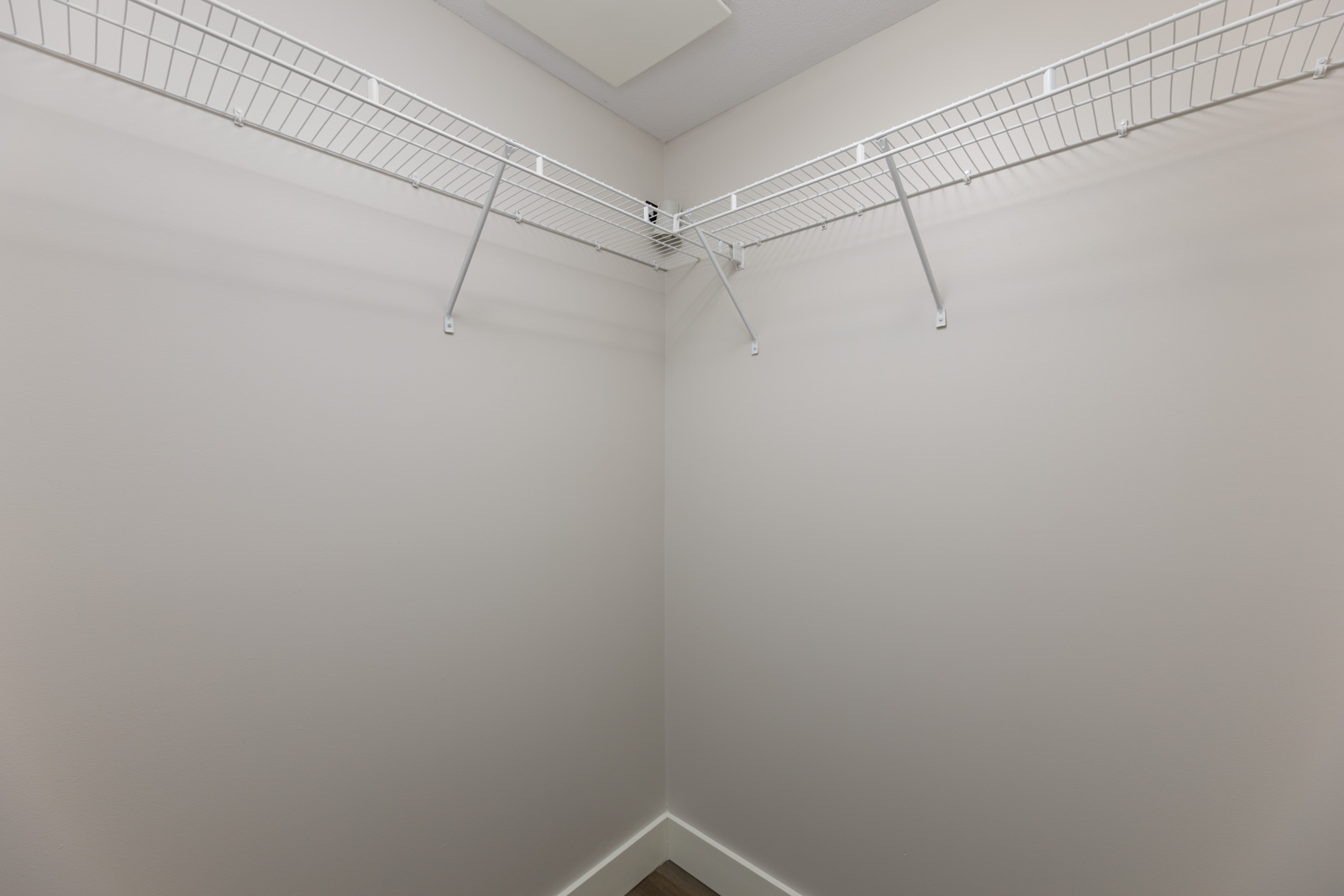 Empty walk-in closet with white walls, two wire shelves attached to the walls, and a plain ceiling.