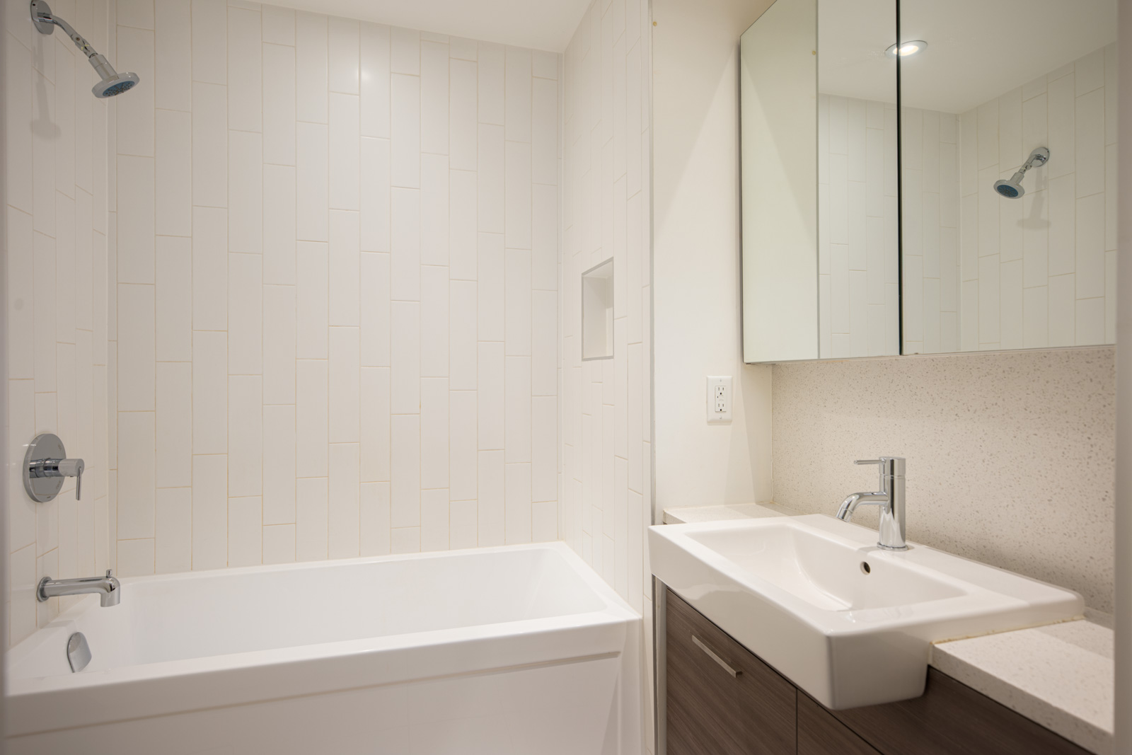 Modern bathroom with a white bathtub, wall-mounted showerhead, rectangular sink with chrome faucet, mirrored cabinet, and light-colored tile walls.