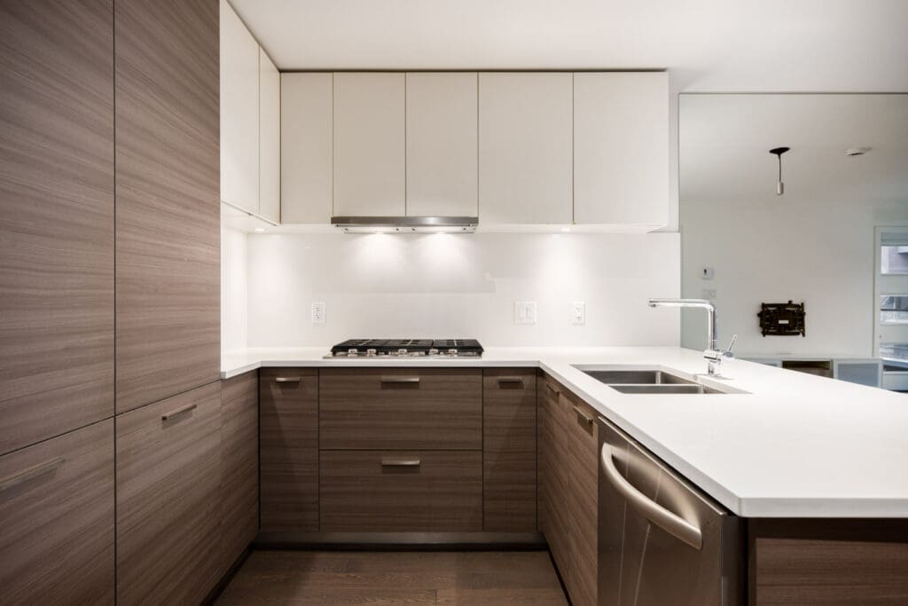 Modern kitchen with wood cabinetry, white countertops, built-in gas stove, stainless steel range hood, and a double sink with a dishwasher beneath.