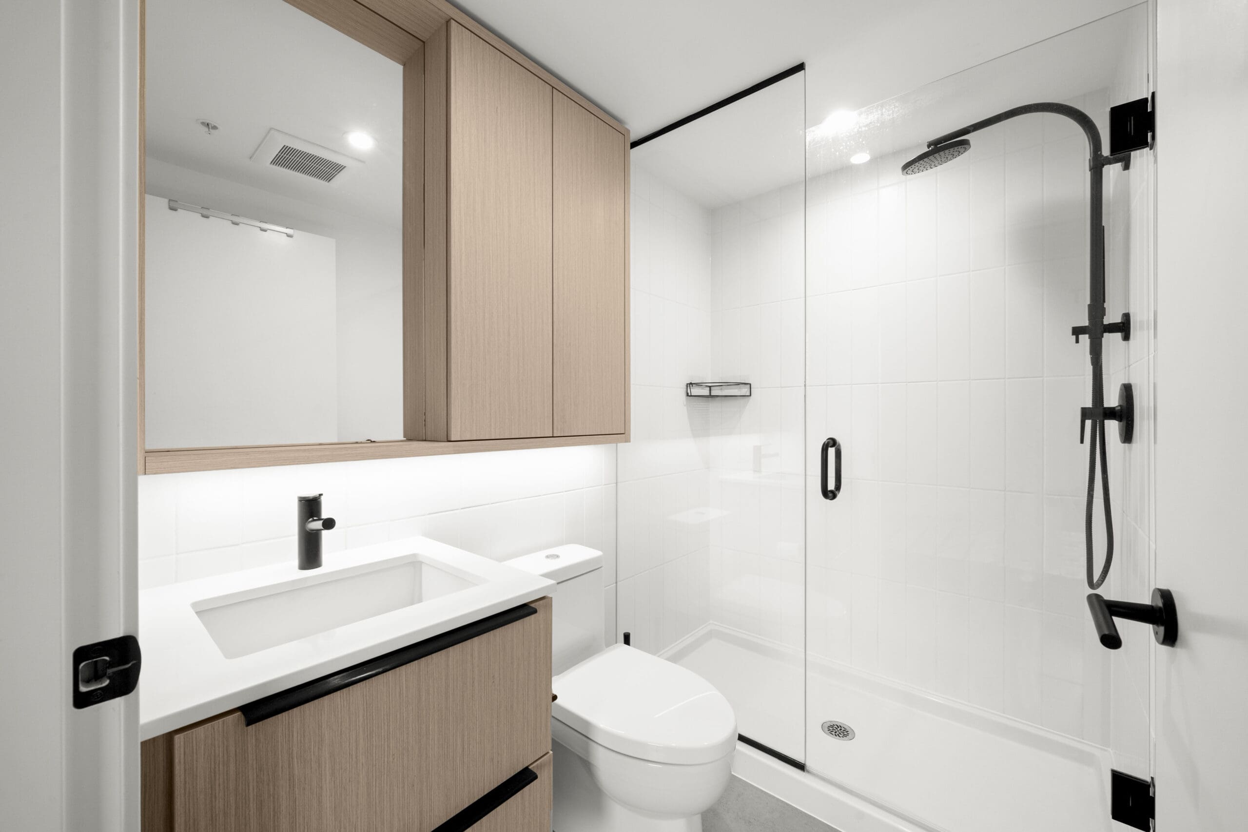 Modern bathroom with a glass-enclosed shower, matte black fixtures, a white vanity with wood cabinets, and a wall-mounted mirror cabinet.