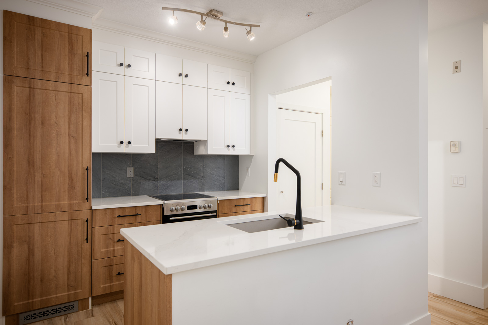 Modern kitchen with white and wood cabinets, black hardware, an electric stove, built-in fridge, marble countertop, and a black faucet on a white island.