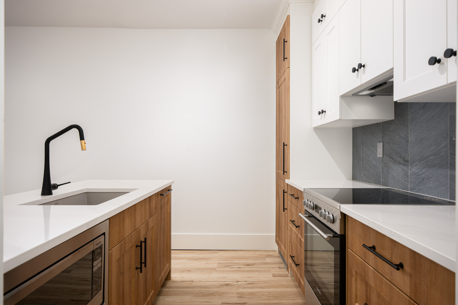 Modern kitchen with white and wood cabinetry, electric stove, built-in oven, under-counter microwave, and a black faucet over a sink on a white countertop.