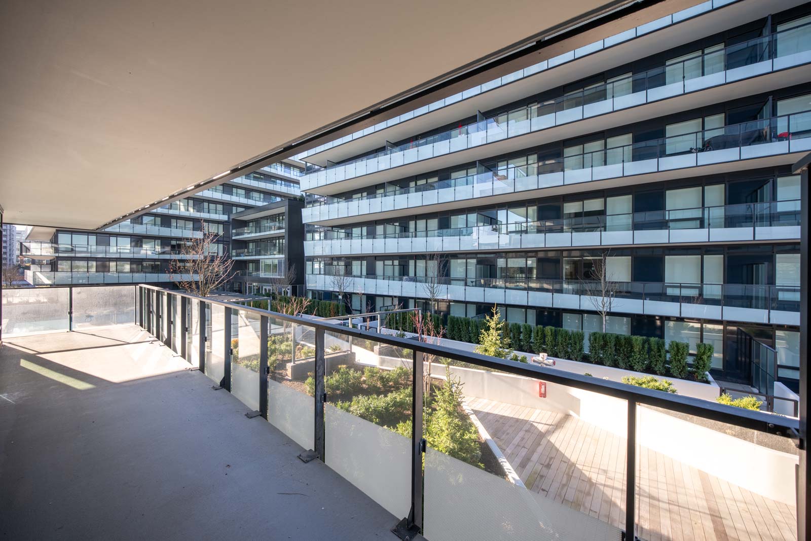 View from a balcony overlooking a landscaped courtyard surrounded by modern apartment buildings with glass railings and balconies.