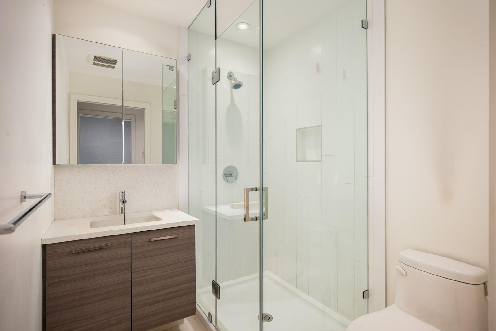 Modern bathroom with a glass-enclosed shower, wall-mounted vanity with sink, mirrored cabinets, and a white toilet.