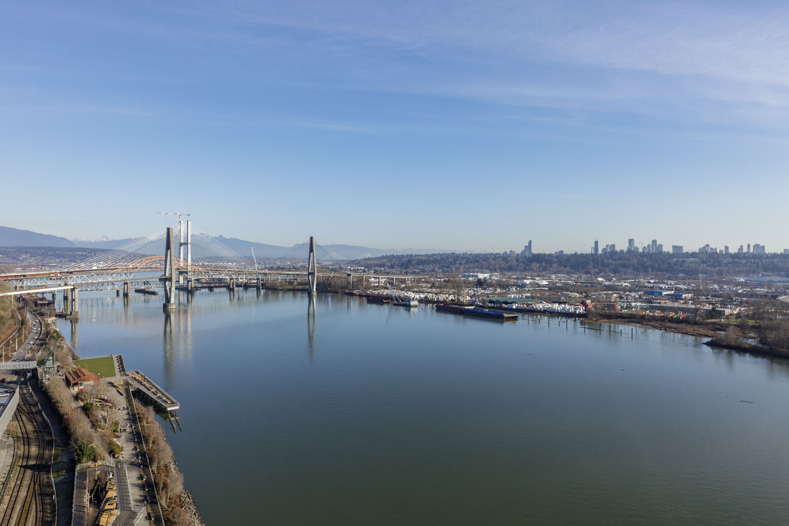 A wide river with a modern cable-stayed bridge and city skyline in the background under a clear blue sky.