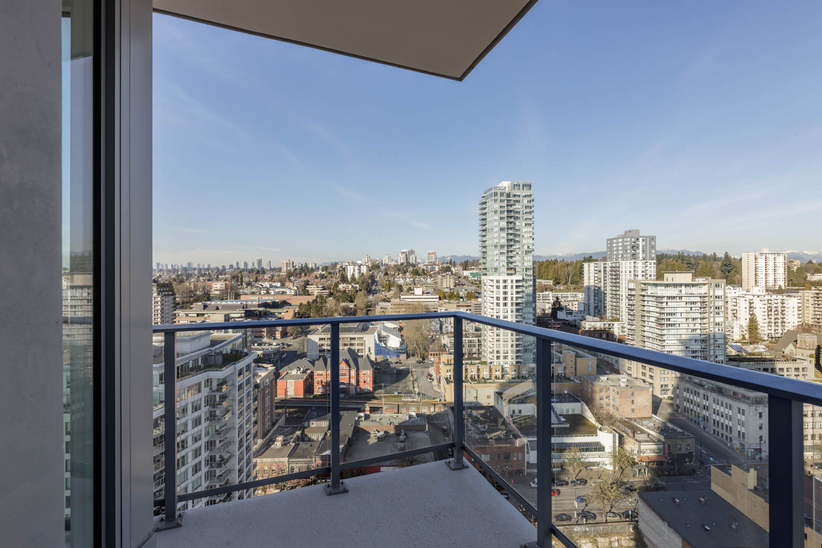 View from a high-rise balcony overlooking a cityscape with several tall buildings under a clear blue sky.