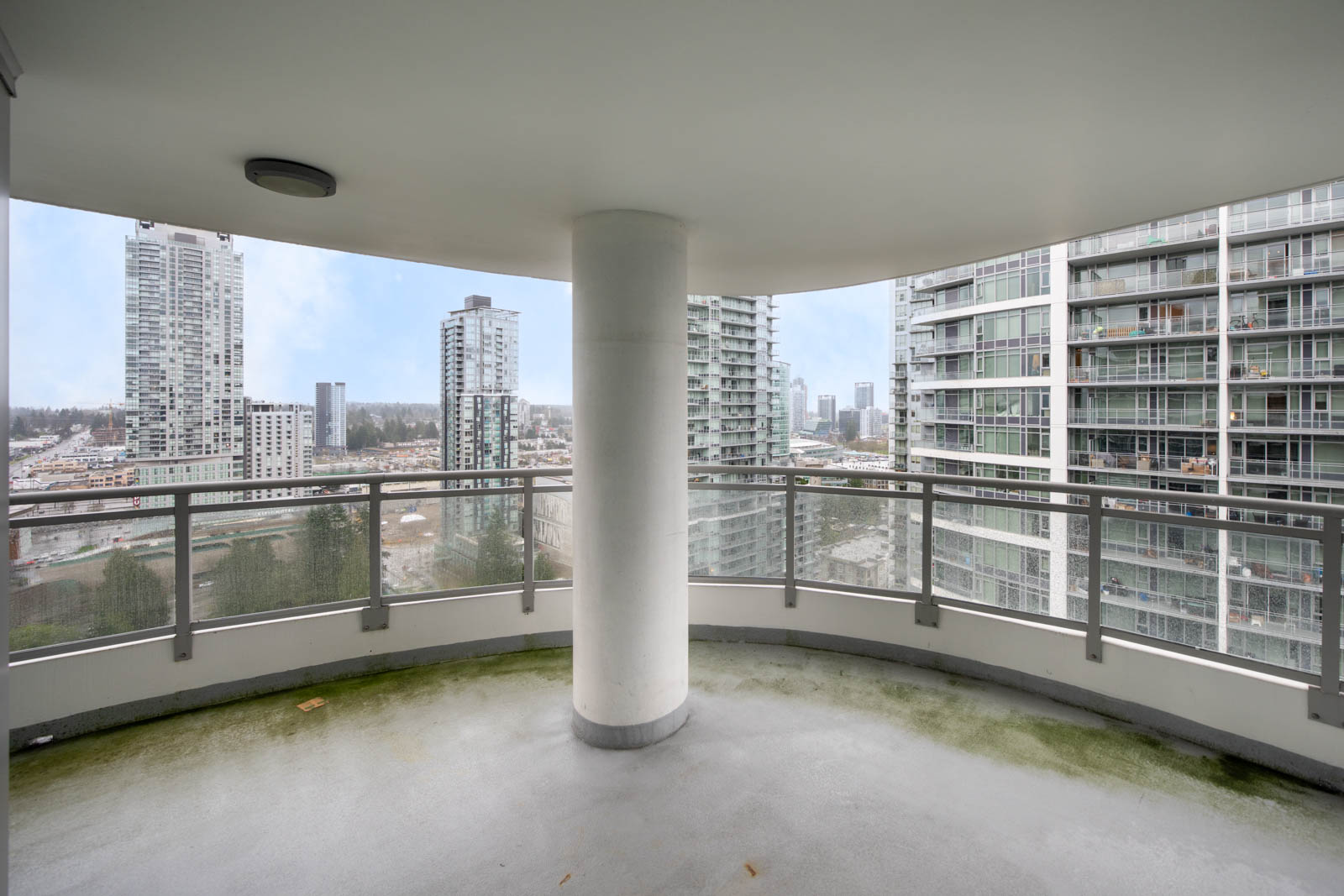 View from a high-rise balcony with glass railings, showing multiple modern apartment buildings and a cityscape in the background.