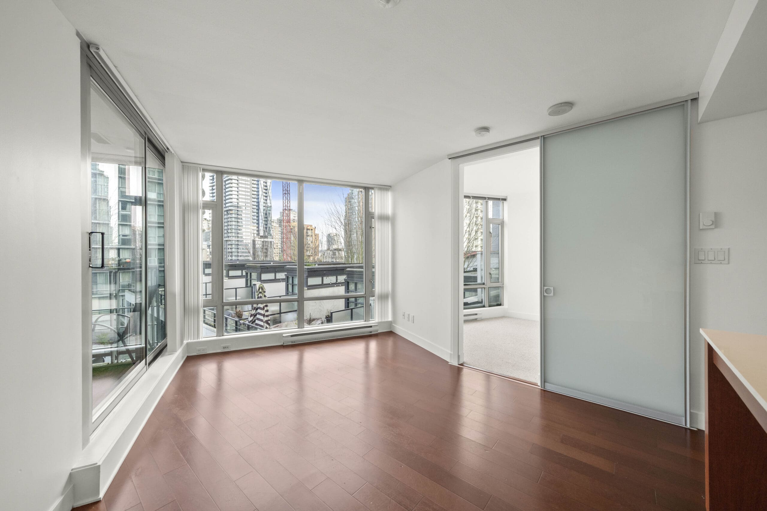Unfurnished modern apartment with large windows, glass sliding doors, hardwood floors, and a city skyline view.