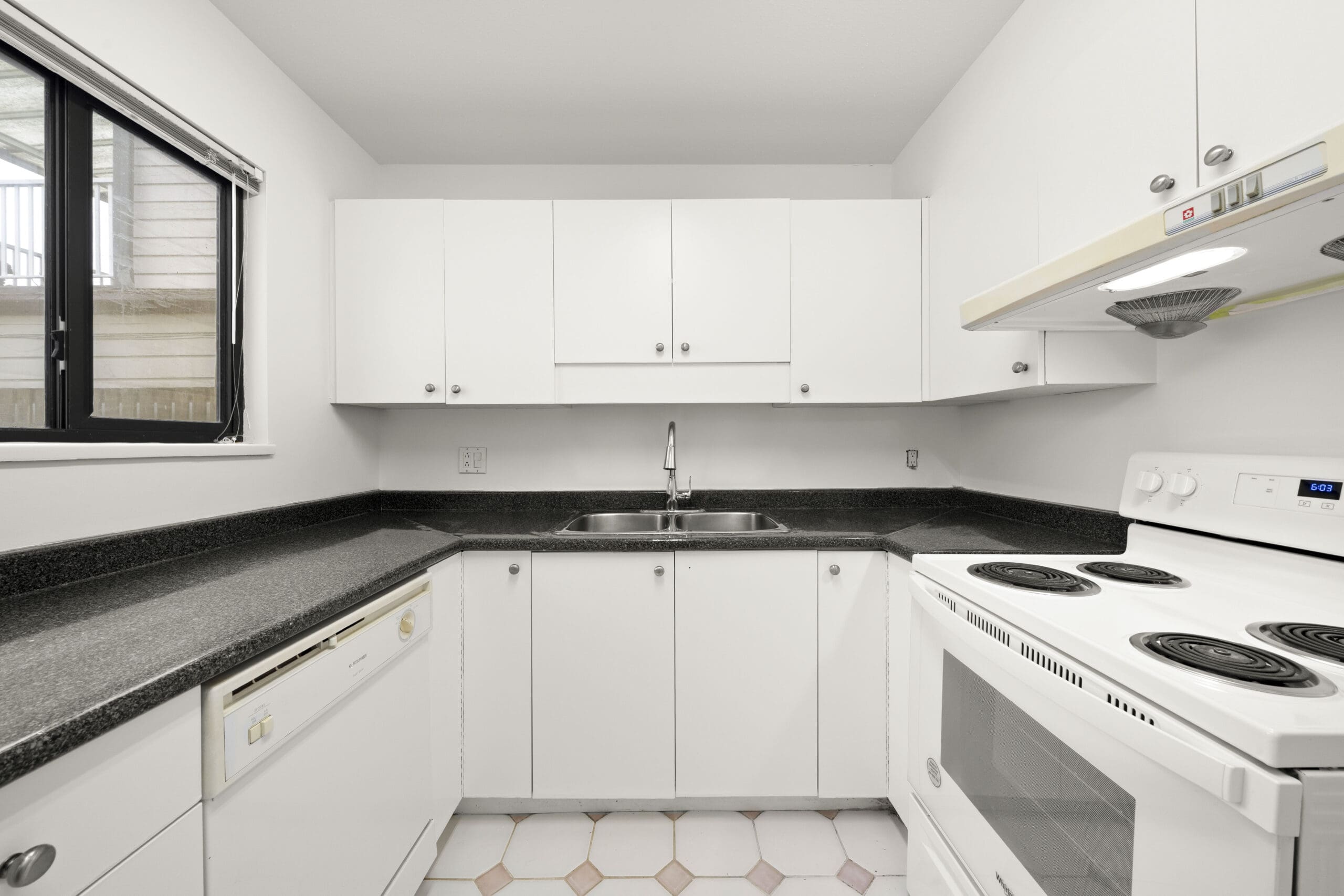 Modern kitchen with white cabinets, black countertops, white electric stove, dishwasher, stainless steel sink, and a window above the countertop.