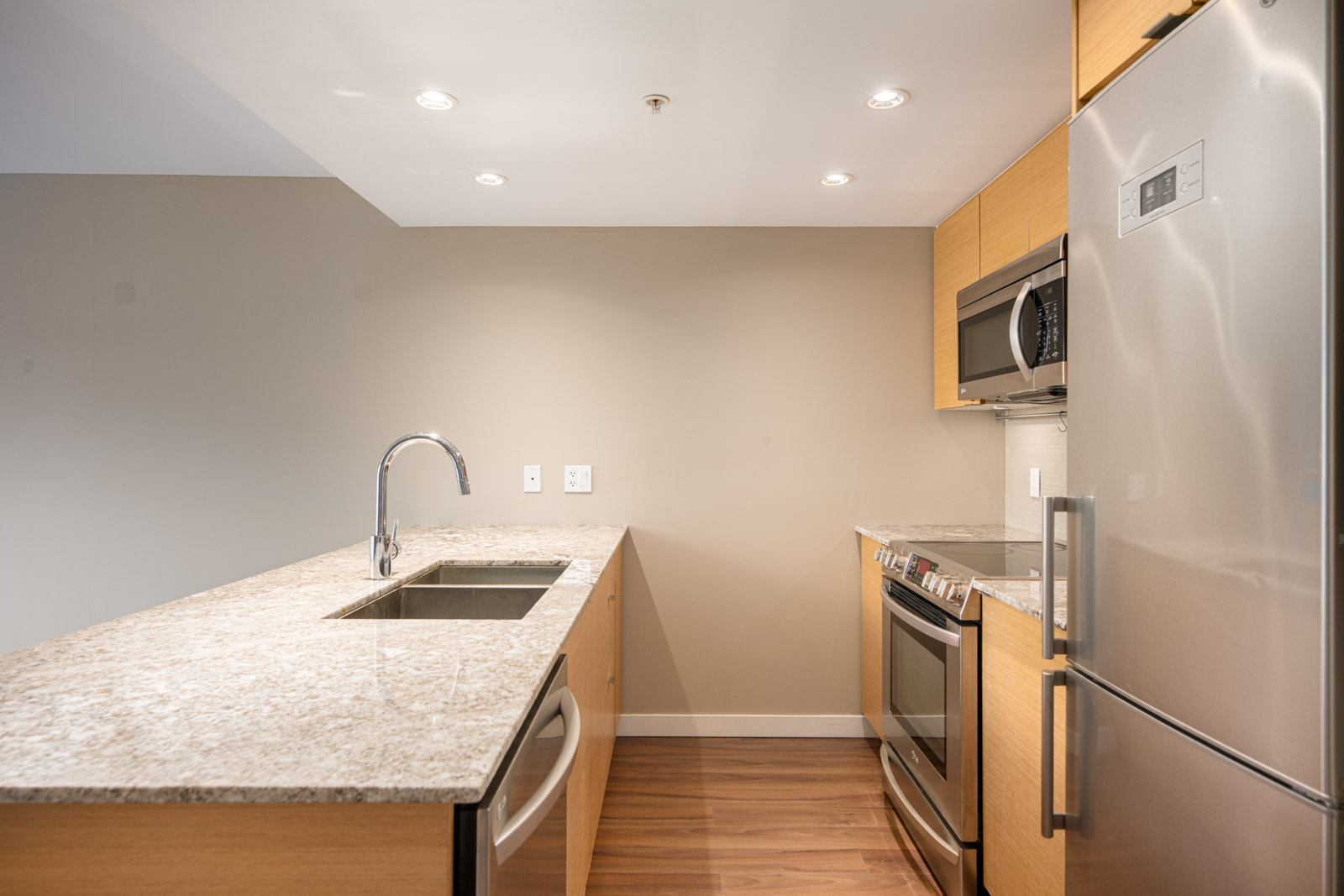 Modern kitchen with granite countertops, stainless steel appliances, built-in microwave, under-mount sink, and light wood cabinets.