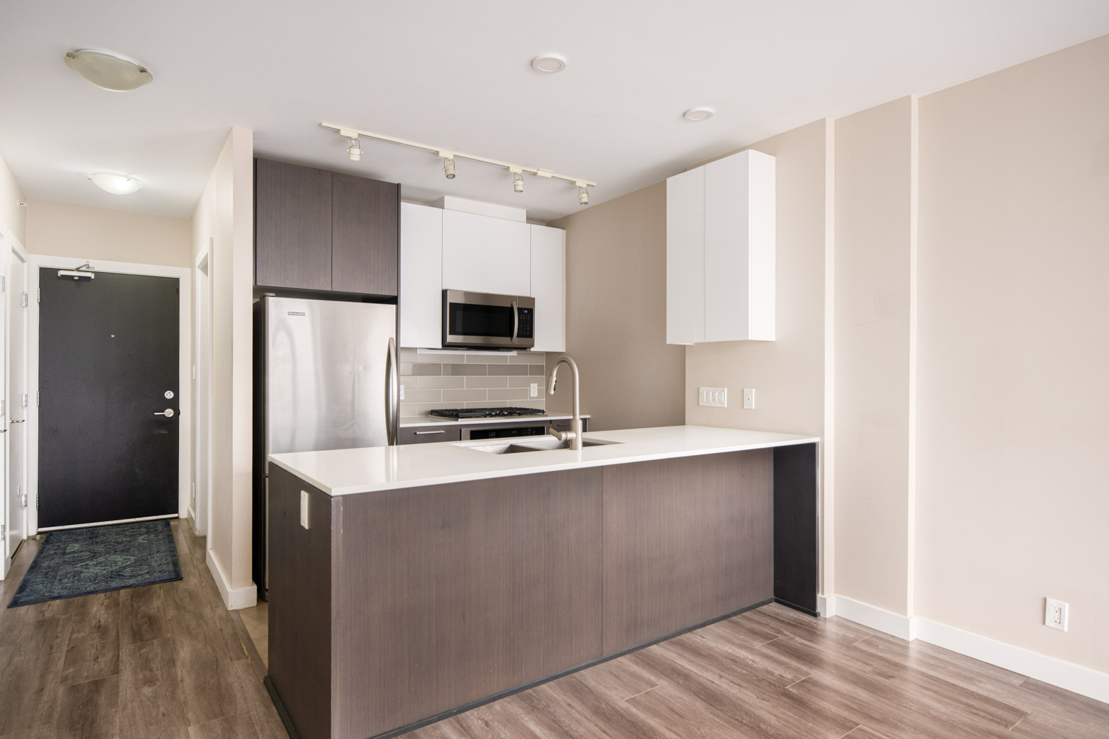 Modern kitchen with stainless steel appliances, dark cabinetry, white countertops, built-in microwave, and an island with a sink. Light wood flooring and neutral walls.