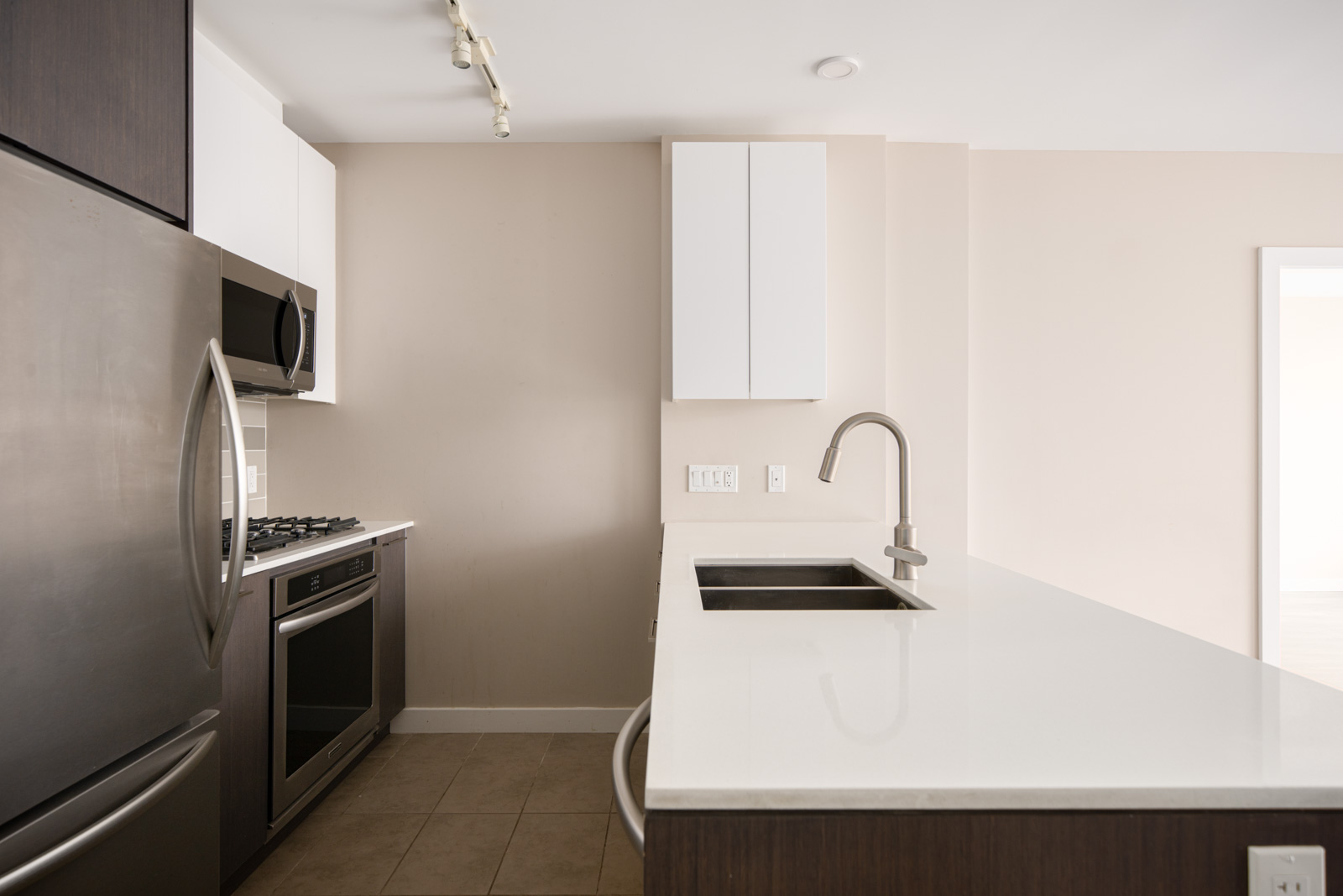 Modern kitchen with stainless steel appliances, white countertops, a built-in oven, gas stove, and an under-mount sink on an island. Neutral walls and tile flooring.