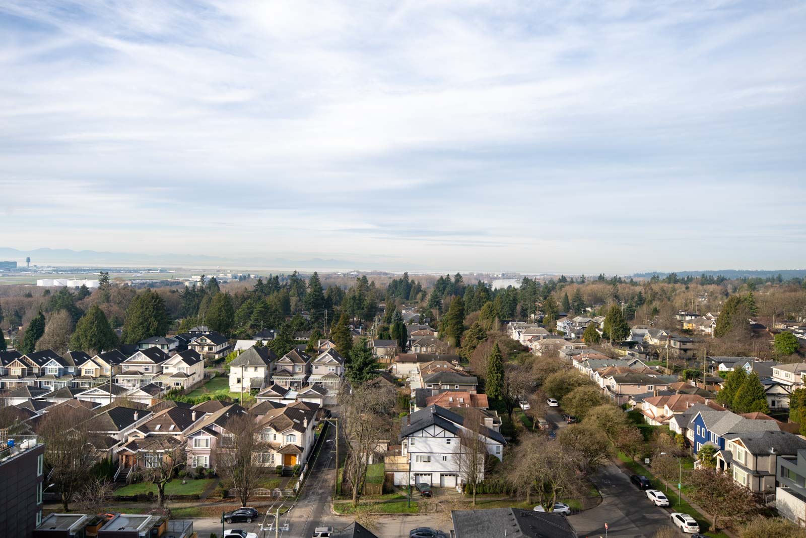 Aerial view of a suburban neighborhood with houses, trees, and roads under a partly cloudy sky.