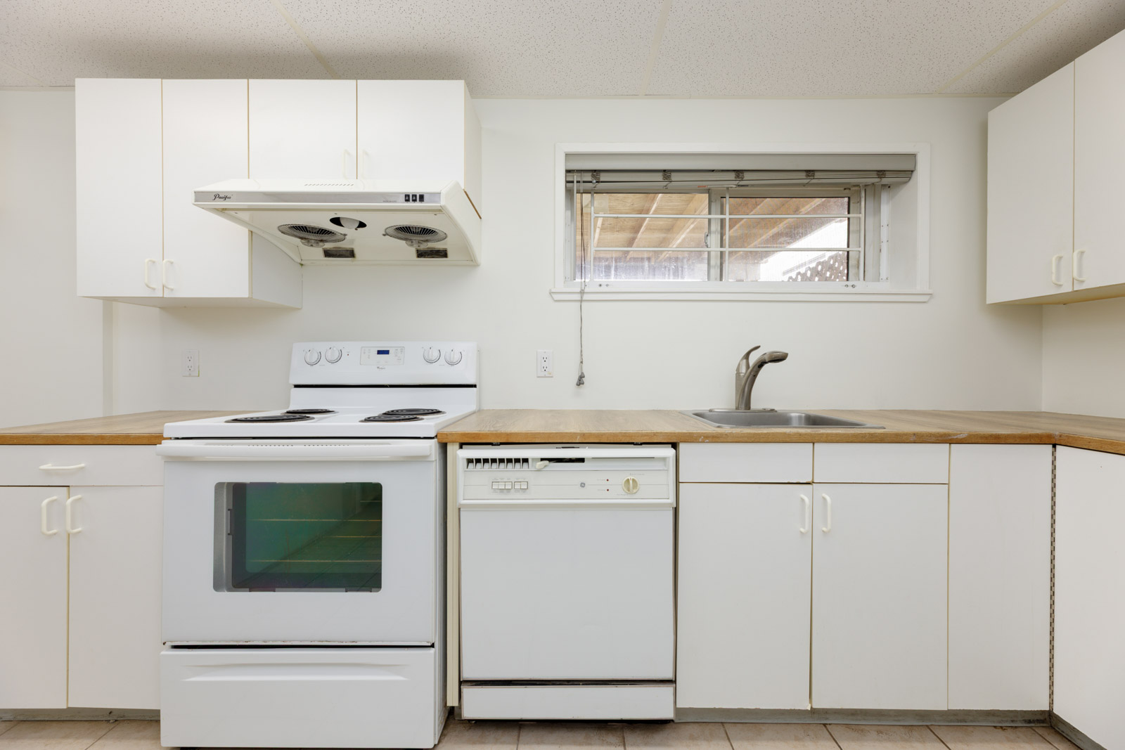 A small kitchen with white cabinets, an electric stove, a range hood, a dishwasher, a sink, and a window above the sink.
