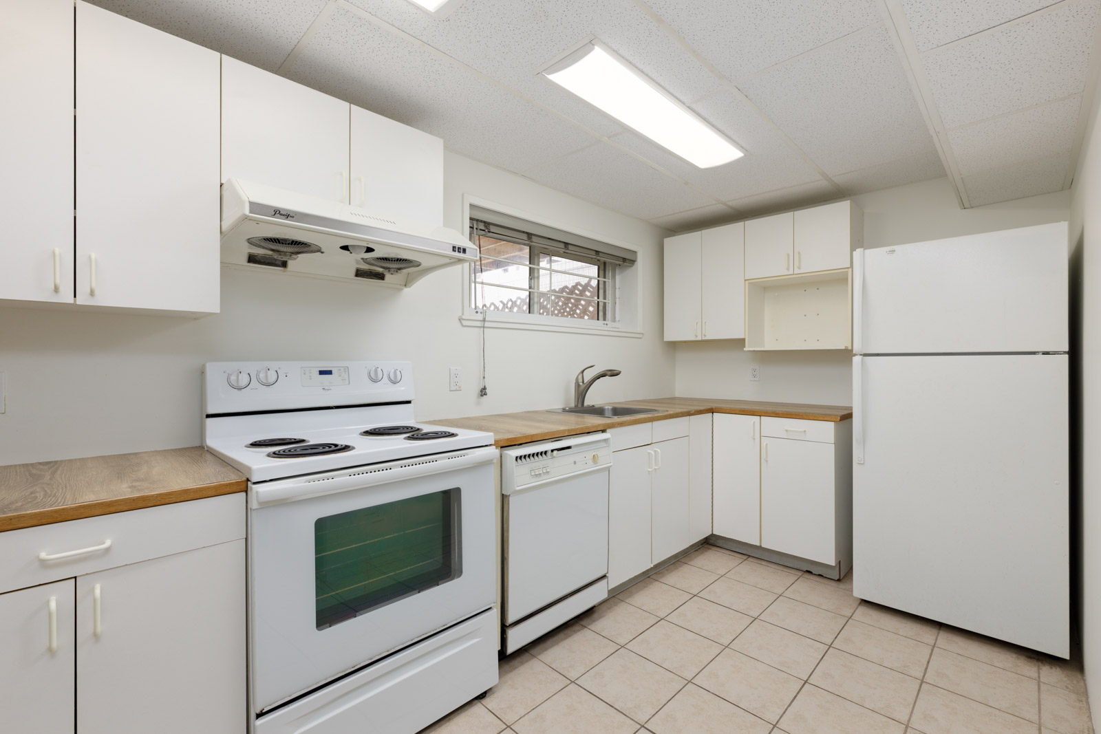 White kitchen with electric stove, range hood, dishwasher, refrigerator, wooden countertops, tiled floor, and overhead fluorescent lighting.