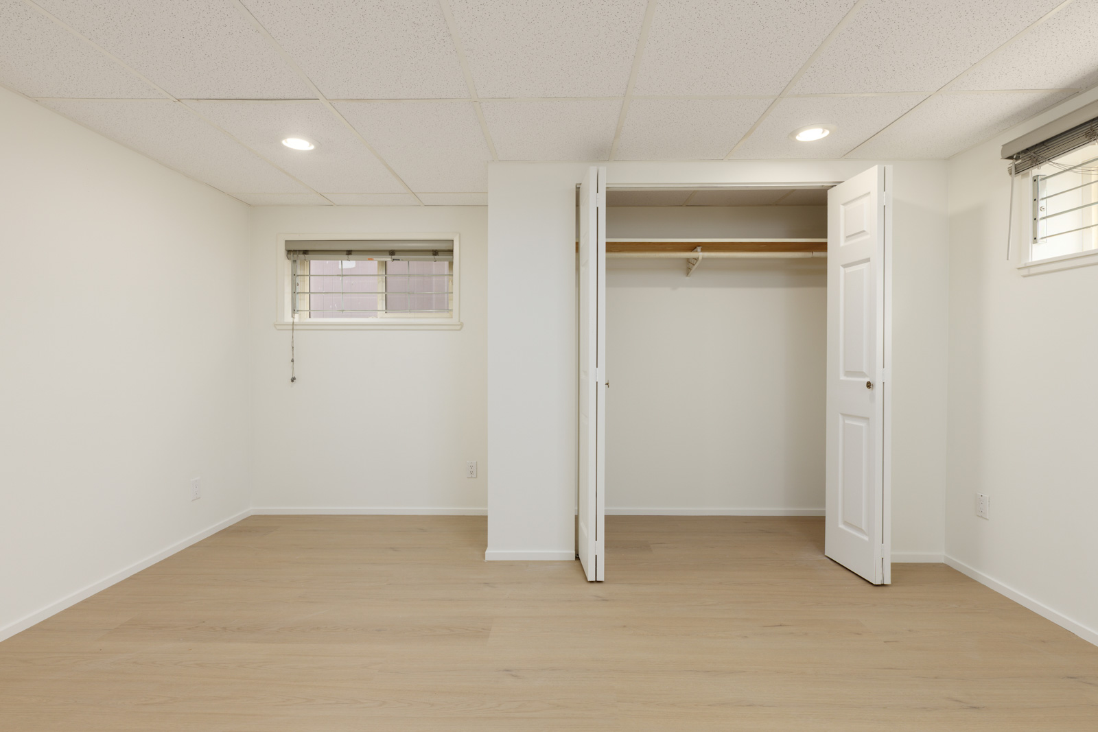Empty room with light wood flooring, white walls, a small window, and an open closet with double doors.
