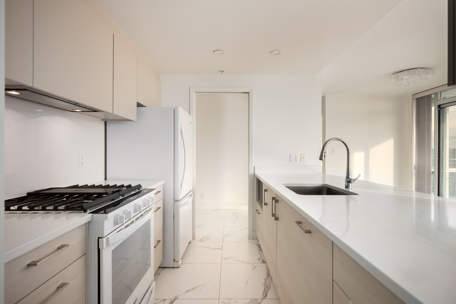 Modern kitchen with white cabinets, gas stove, refrigerator, under-mount sink, and marble tile floor, featuring a clean and minimal design.