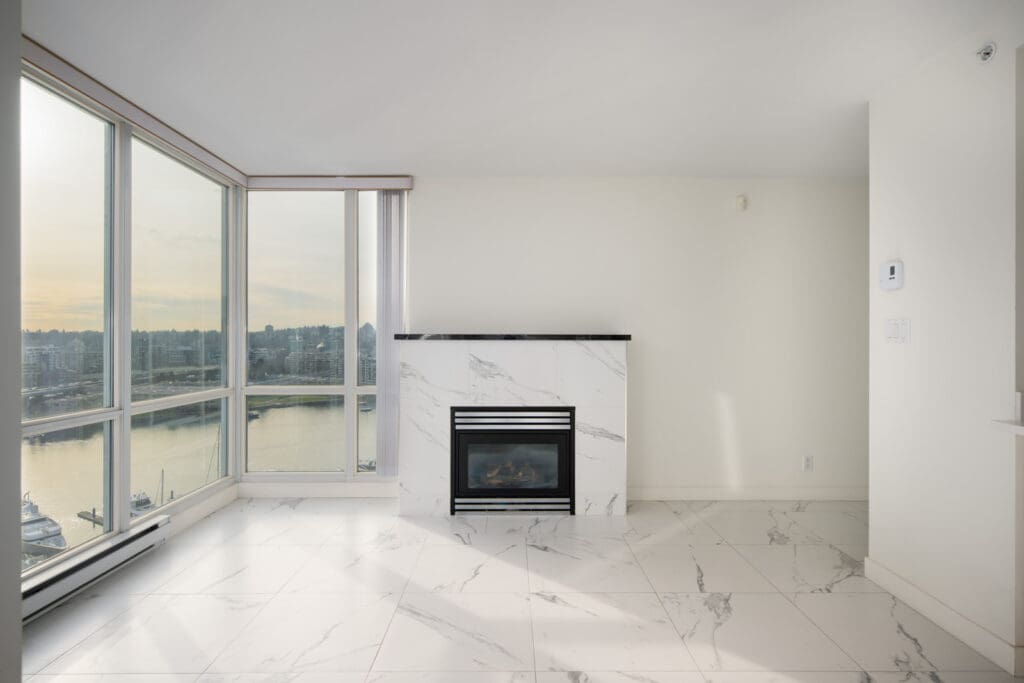 Bright, modern living room with large windows, marble tile flooring, and a marble fireplace overlooking a waterfront view.