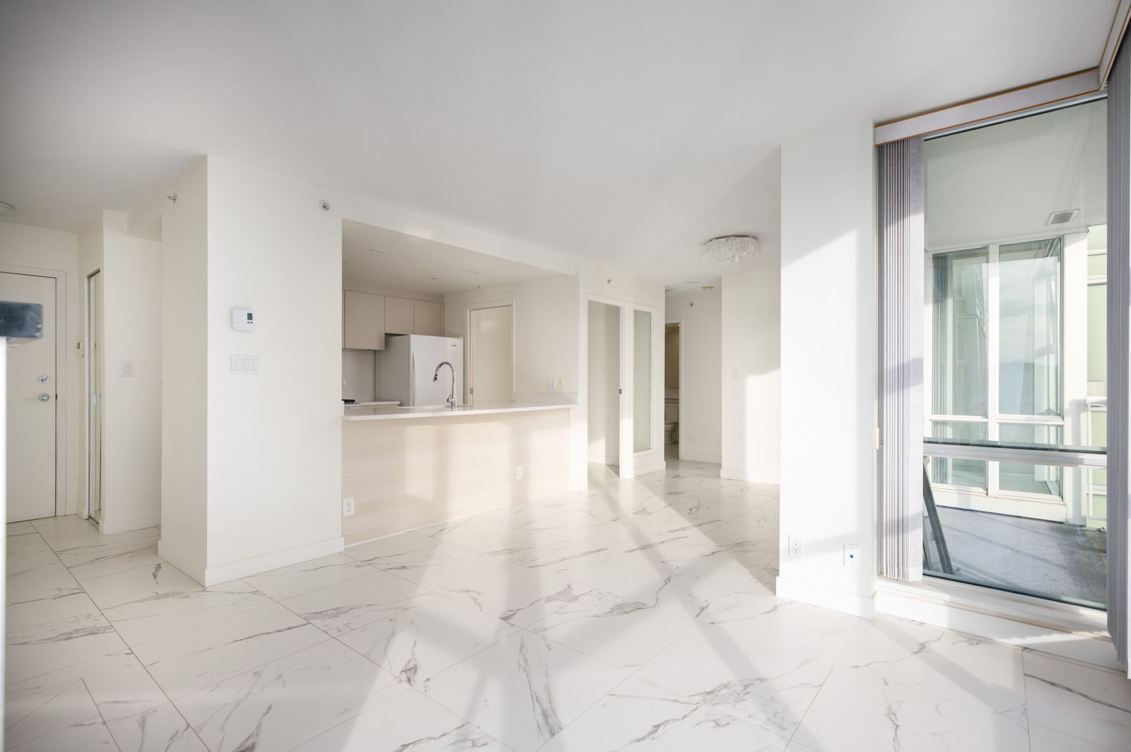 Bright, modern apartment interior with white marble floors, open kitchen, minimalist cabinetry, and large windows letting in natural light.