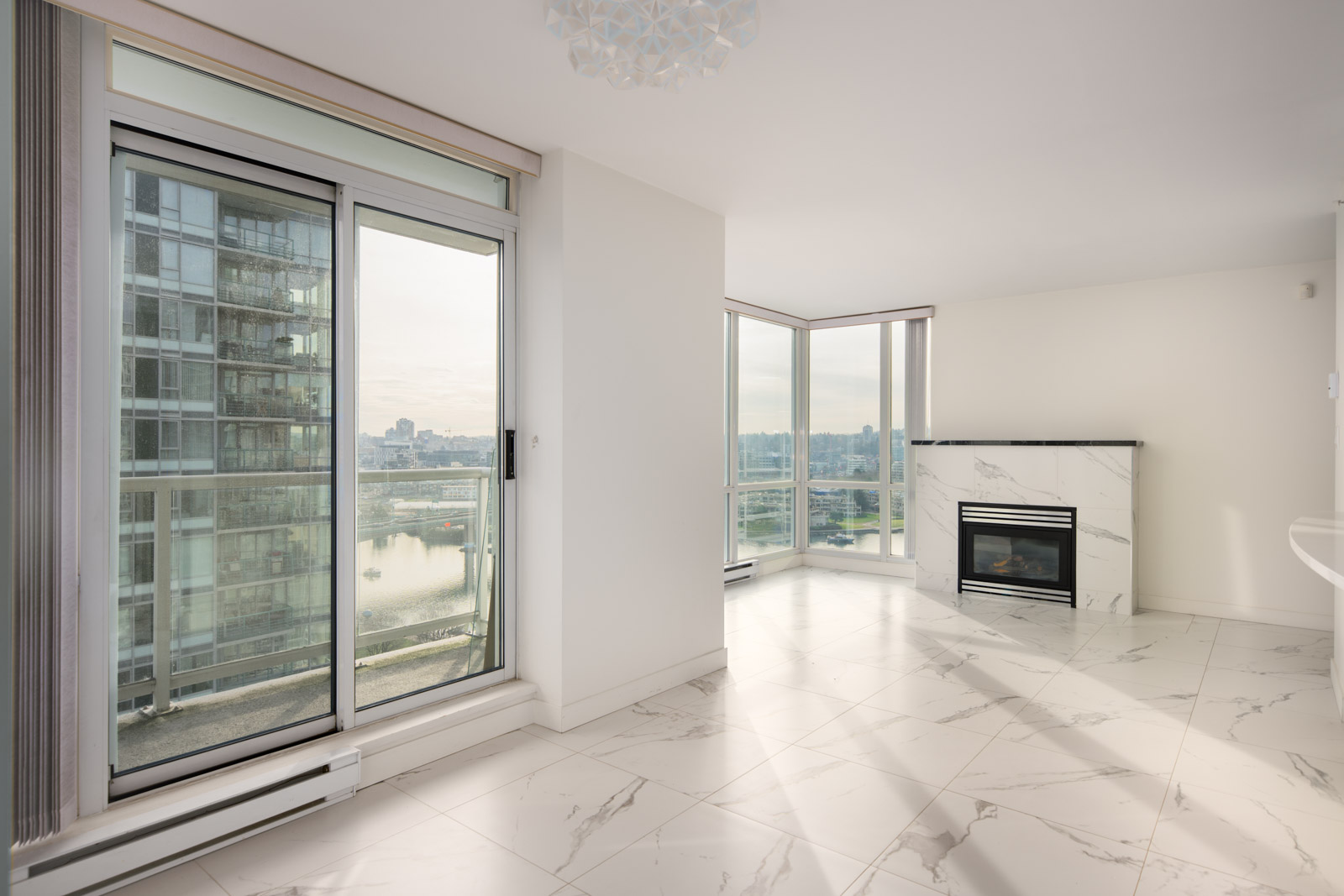 Modern empty apartment with large windows, marble tile flooring, a fireplace, and a view of the city and waterfront from a high floor.