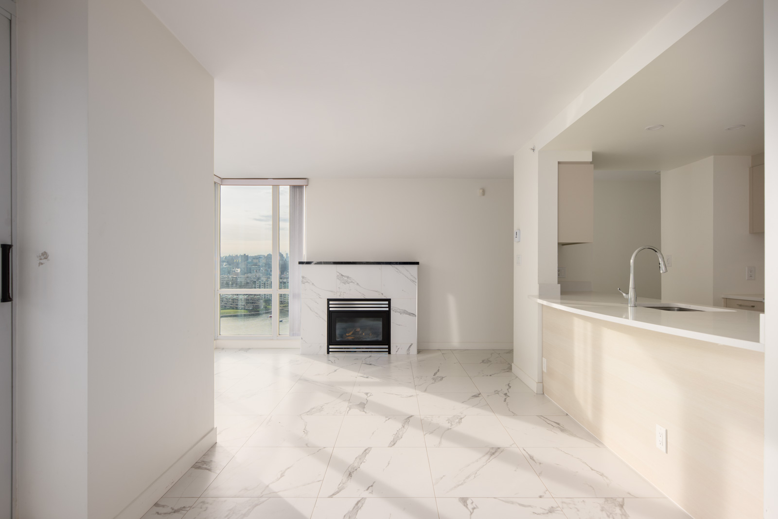 Bright, modern apartment interior with large window, marble tile floors, a built-in fireplace, and an open kitchen with light cabinets and a sink.