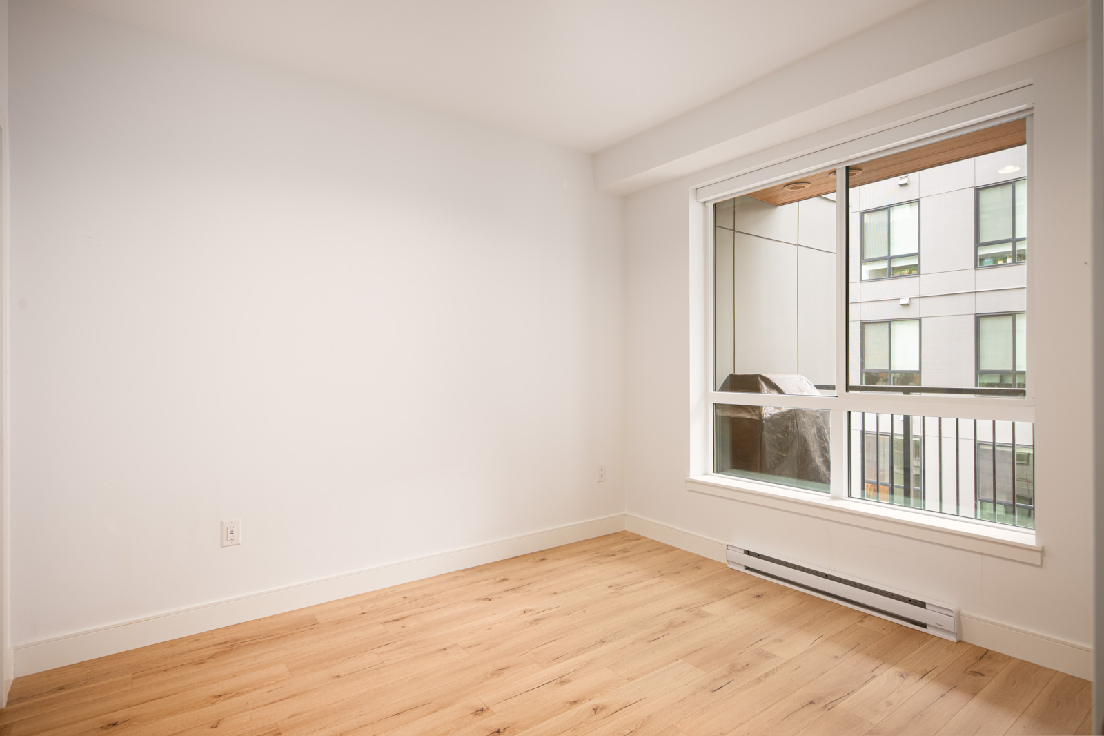 Unfurnished room with light wood flooring, white walls, a large window, and a baseboard heater beneath the window.