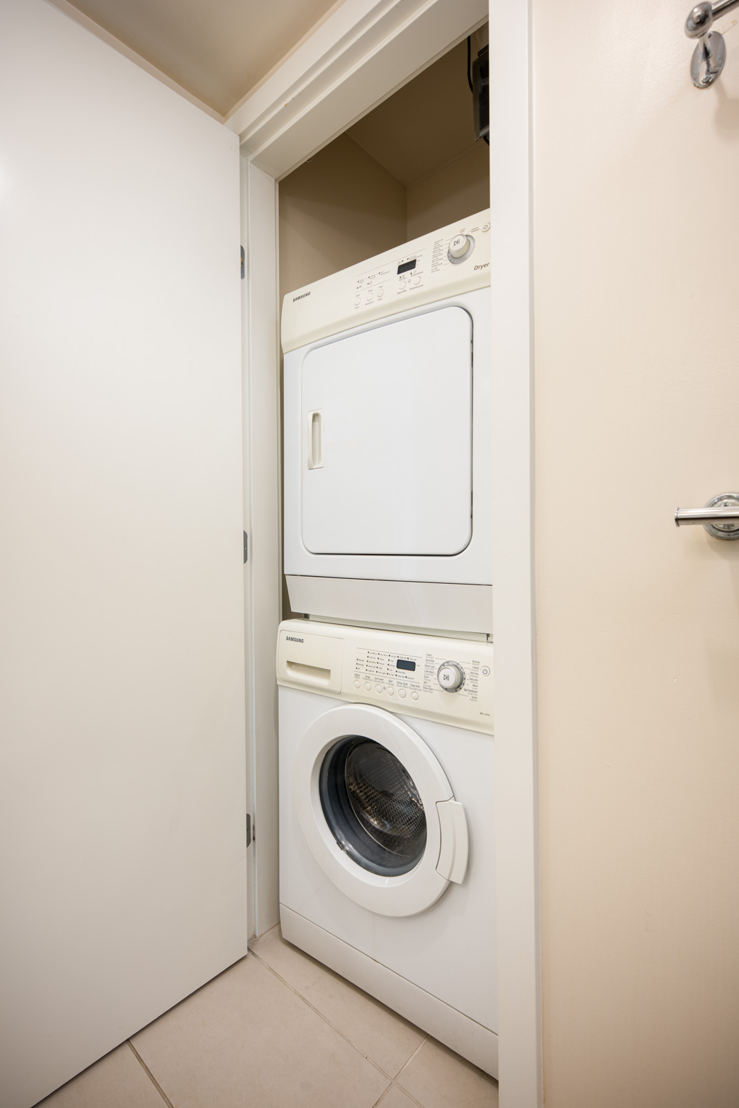 A stacked washer and dryer set in a small, white closet with the door partially open.