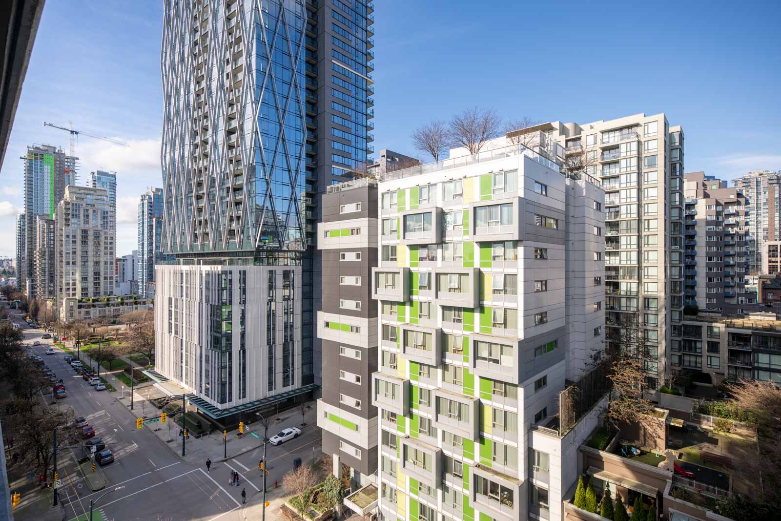High-rise residential and commercial buildings line a city street intersection under a clear blue sky.