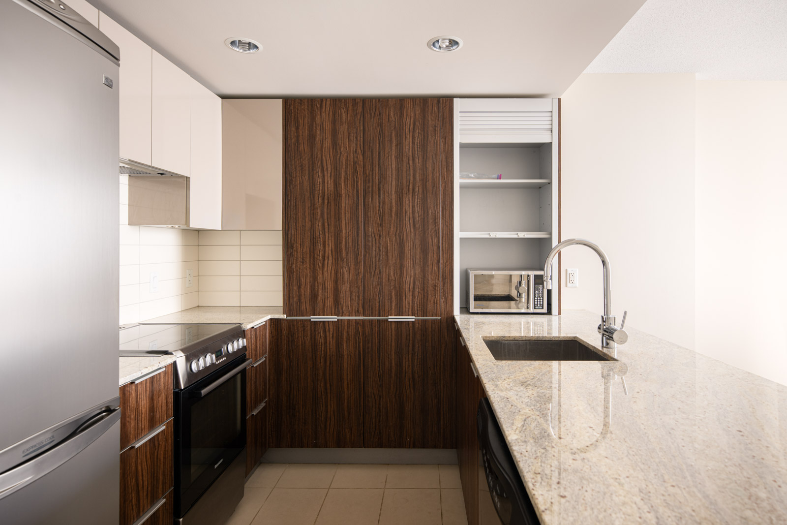Modern kitchen with wood-paneled cabinets, stainless steel appliances, a built-in microwave, tile backsplash, and a granite countertop with an undermount sink and faucet.