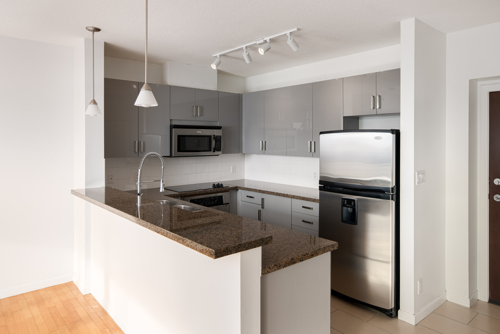 Modern kitchen with gray cabinets, stainless steel appliances, granite countertop, and pendant lighting, featuring a built-in microwave and double-door refrigerator.