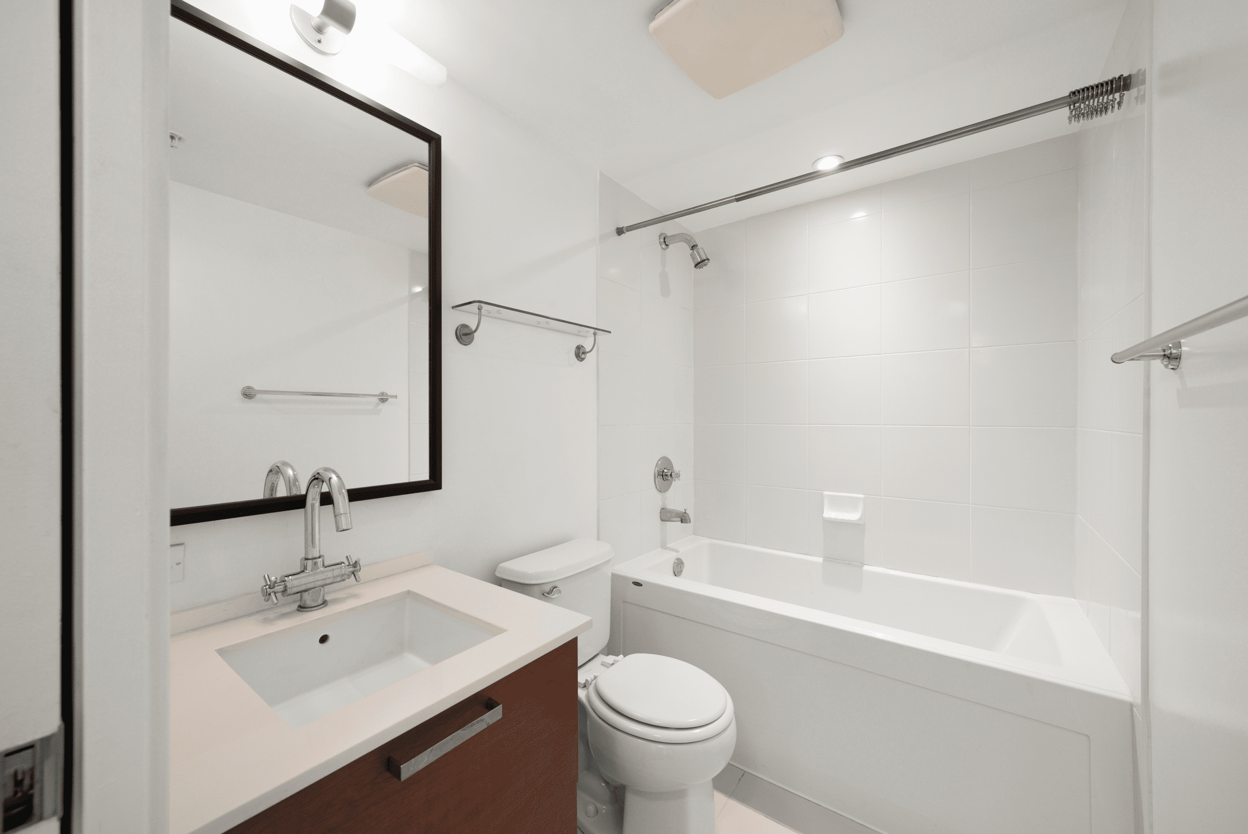 Modern bathroom with a white bathtub-shower combo, toilet, vanity with sink and faucet, large mirror, and minimal wall-mounted shelves.