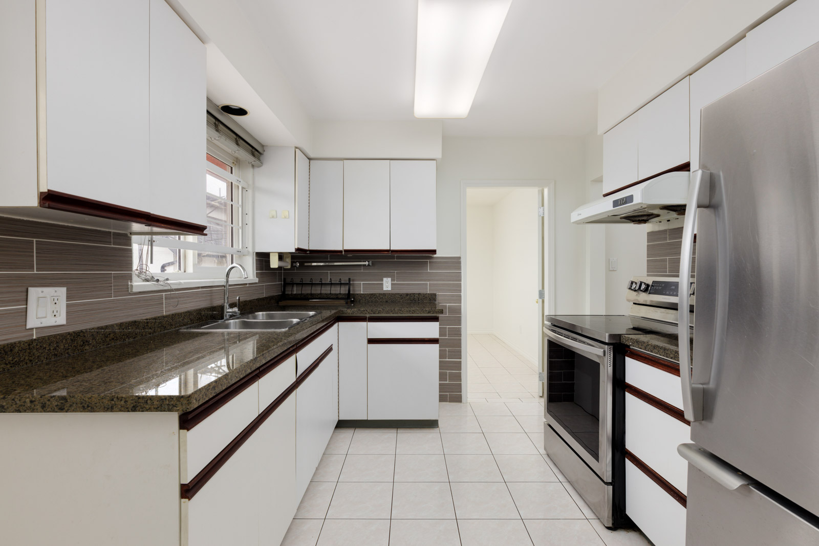 Modern kitchen with white cabinets, brown countertops, stainless steel appliances, tiled floor, and a window above the sink.