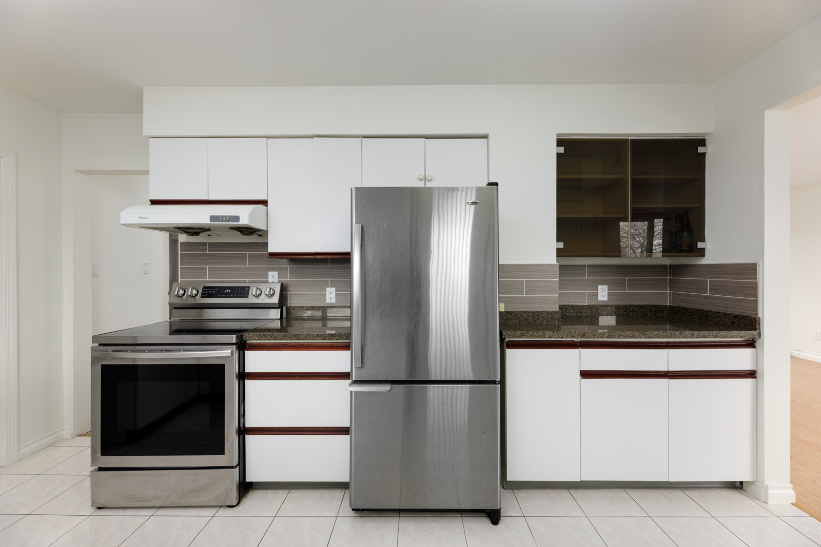 Modern kitchen with stainless steel refrigerator and oven, white cabinets, tile floor, and a gray tiled backsplash.