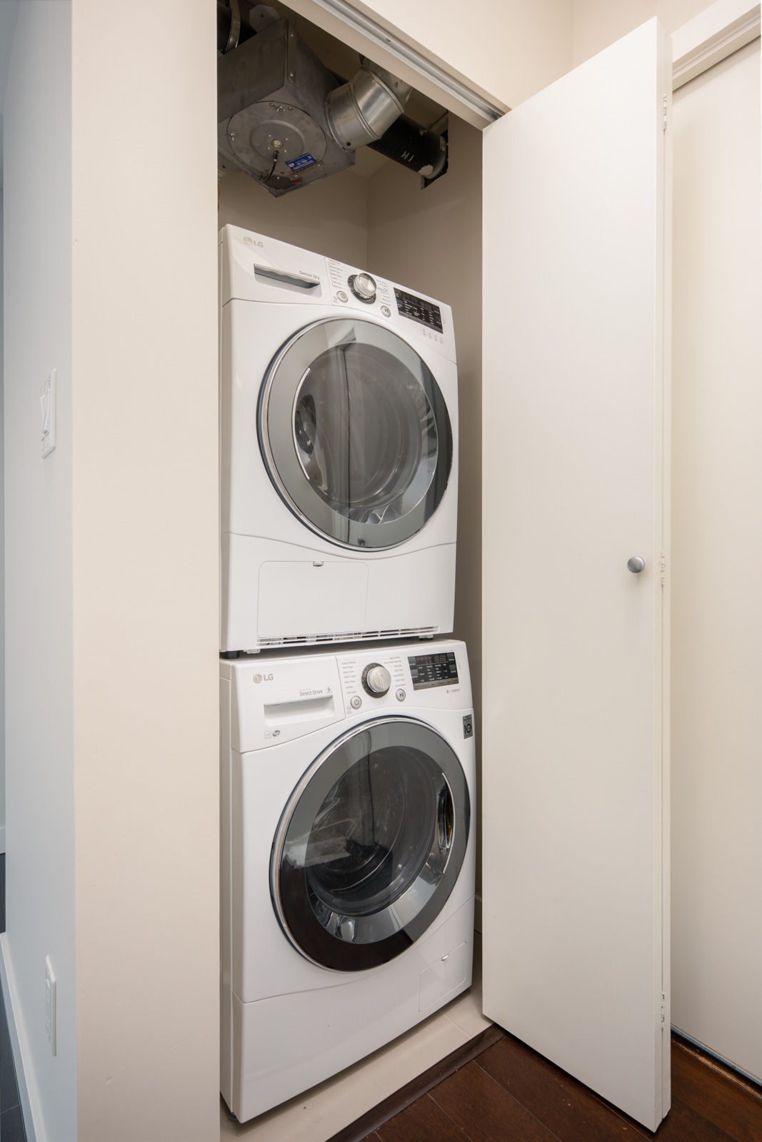 A stacked washer and dryer set is installed in a small closet with white walls and a partially open door.
