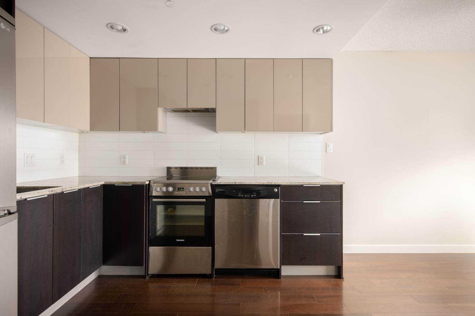 Modern kitchen with beige upper cabinets, dark lower cabinets, stainless steel appliances, and white tile backsplash.