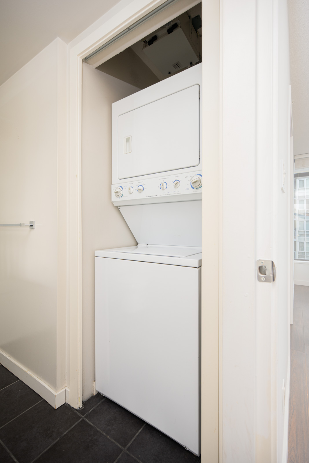 Stacked washer and dryer unit installed in a small closet space with white walls and a tiled floor.