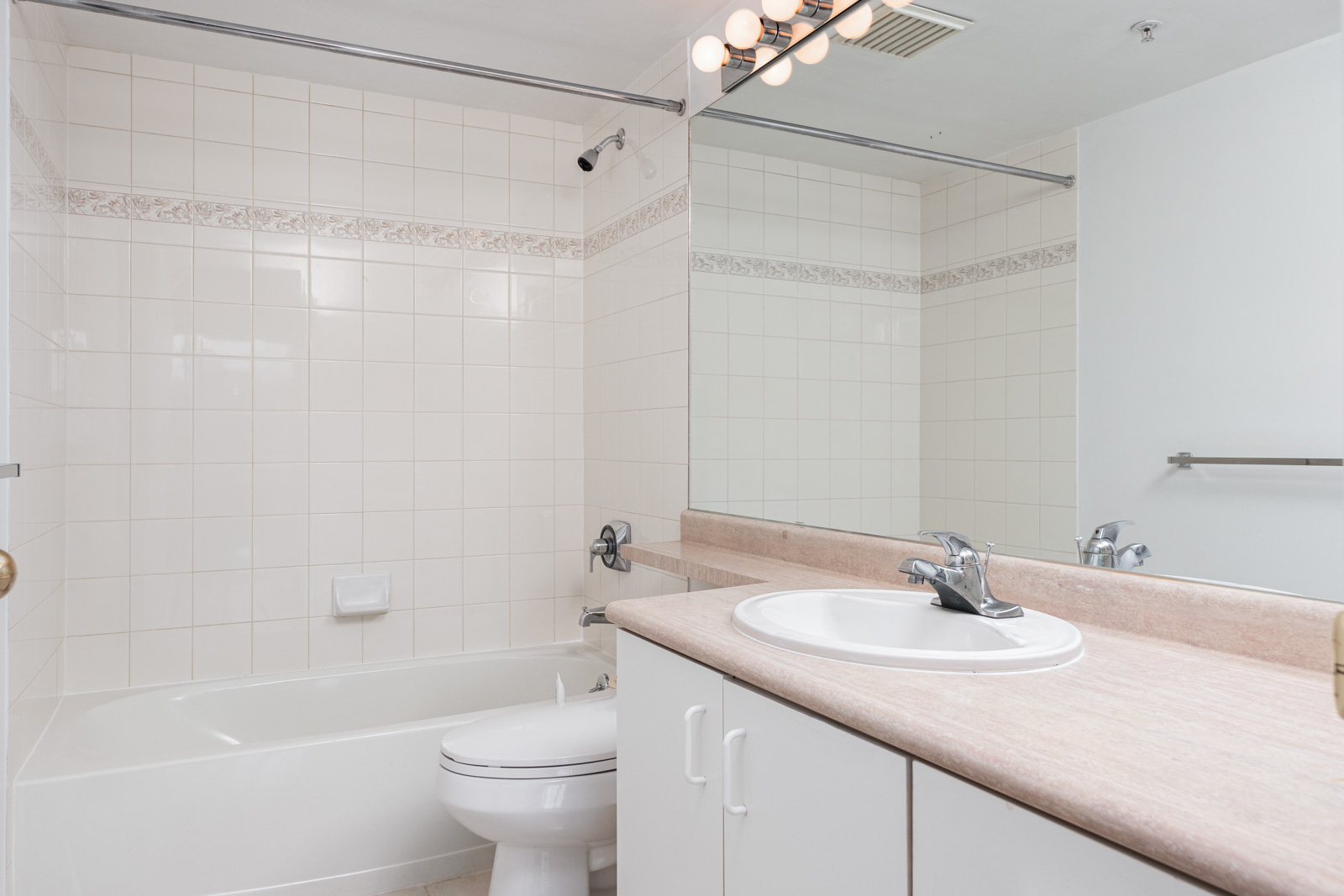 Bathroom with a bathtub and shower, toilet, single sink with countertop, large mirror, and tiled walls with a decorative border.