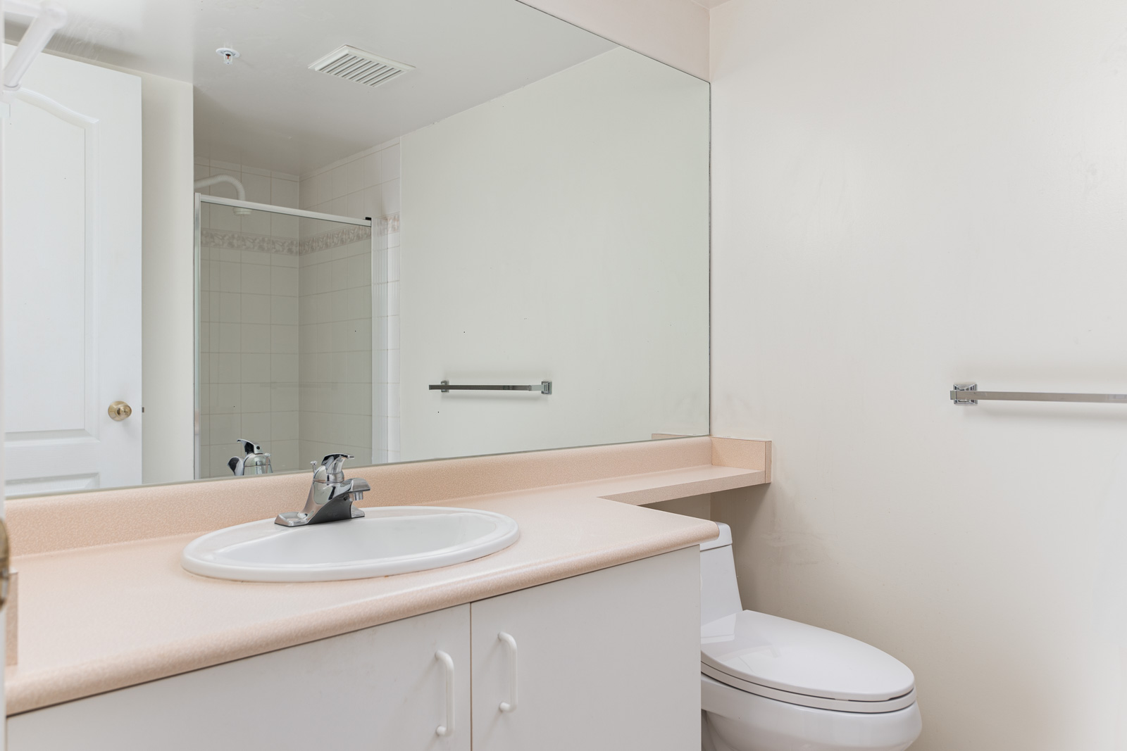 Bathroom with a large mirror, white sink, countertop, toilet, towel rack, and a shower with a glass door in the background.