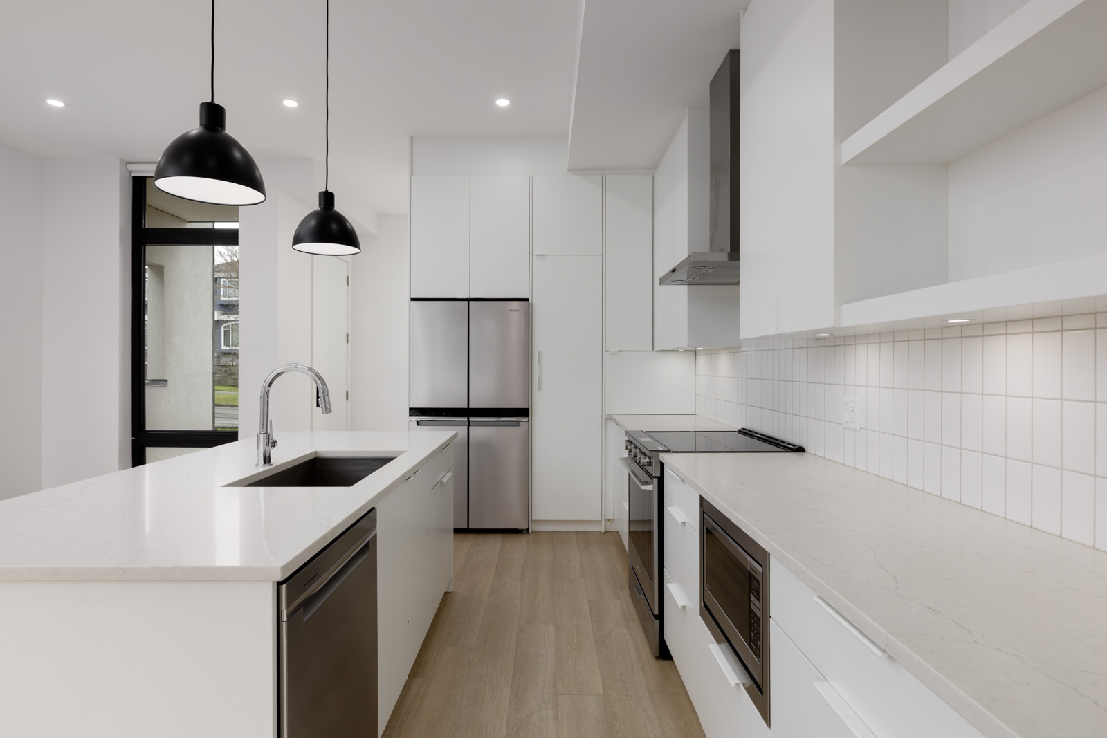 Modern kitchen with white cabinets, stainless steel appliances, pendant lights, an island with a sink, and light wood flooring.