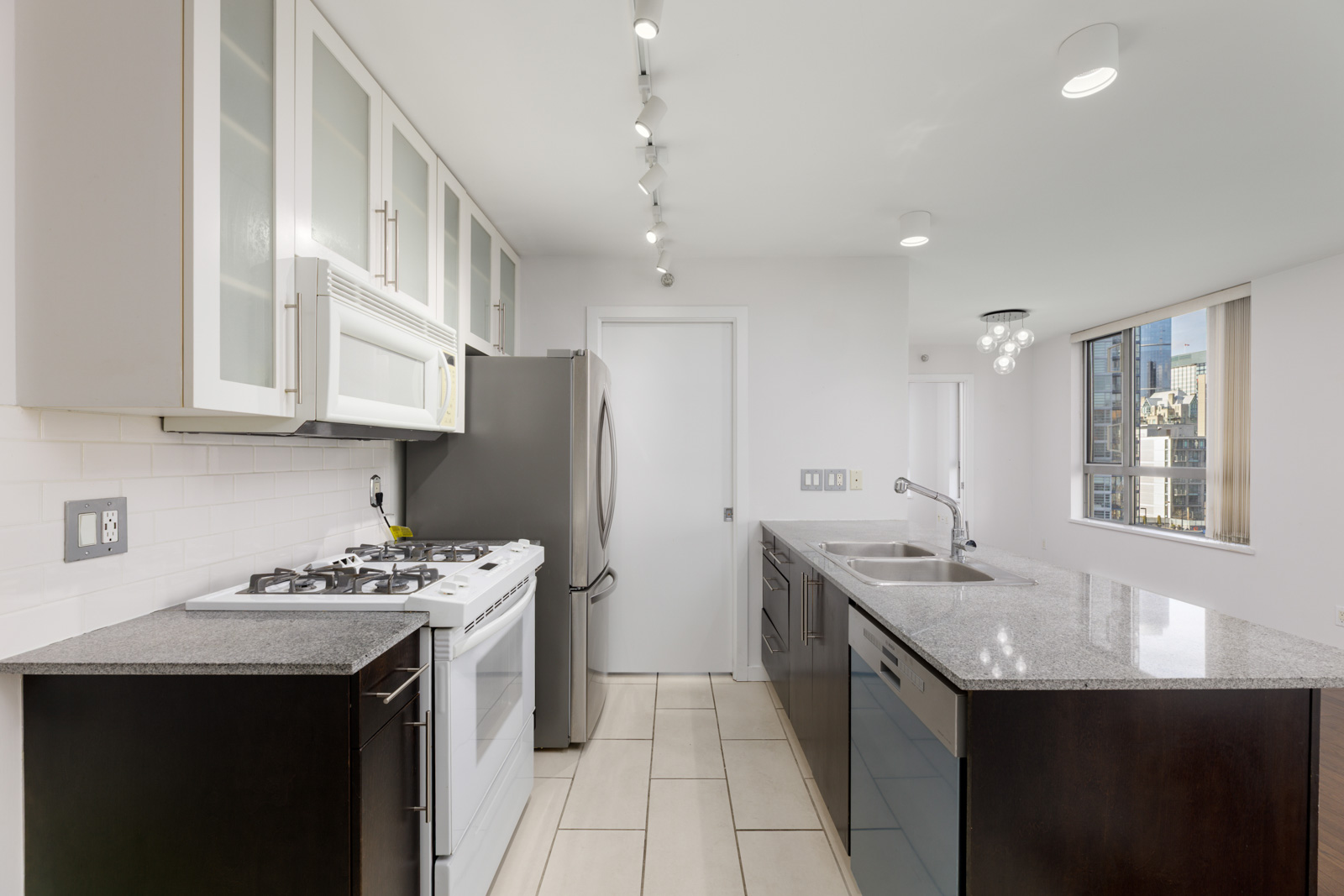 Modern kitchen with white cabinets, stainless steel appliances, double sink, and large window providing city views.