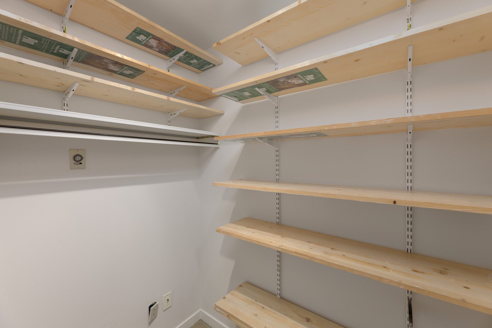 Empty storage room with multiple wooden shelves mounted on white walls and a closet rod on the left side.