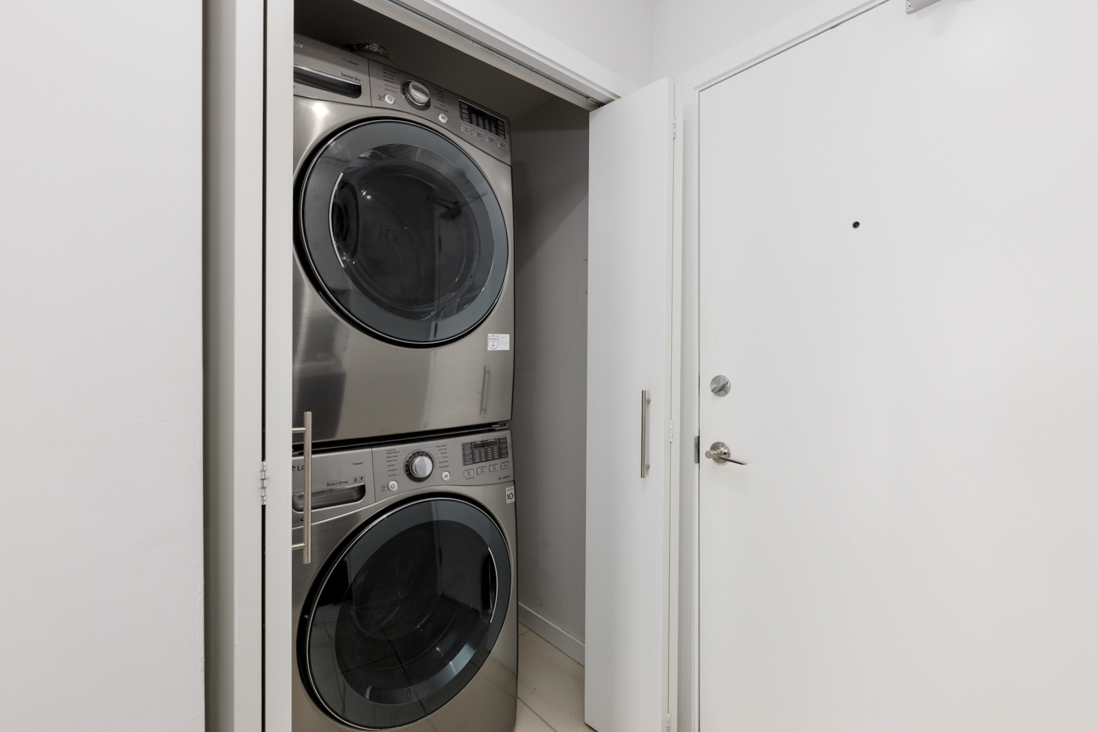 Stacked front-loading washer and dryer units in a small laundry closet with white walls and open doors.