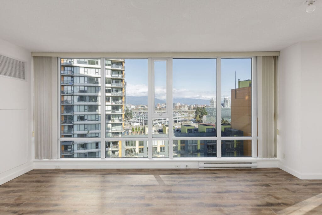 Unfurnished room with large floor-to-ceiling windows, wood flooring, and a cityscape view featuring modern buildings and mountains in the background.